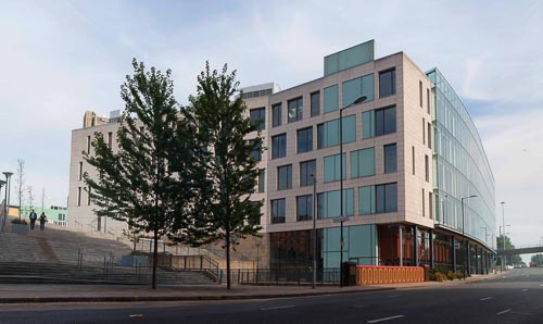 The glass and concrete exterior of the MIB, with a road lined with trees running alongside it.
